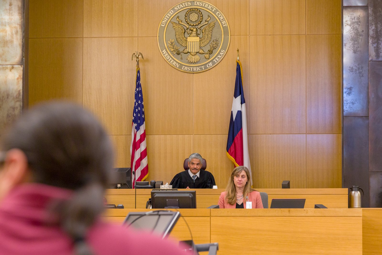 A federal courtroom in the Western District of Texas, with the court seal mounted above the bench and the United States and Texas flags beside it.